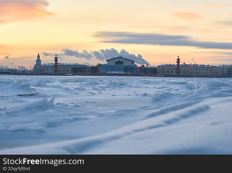 A winter view of Vasilyevsky Island Spit and the Stock Exchange across the snowy, frozen bank of the Neva River. Bright orange-pin