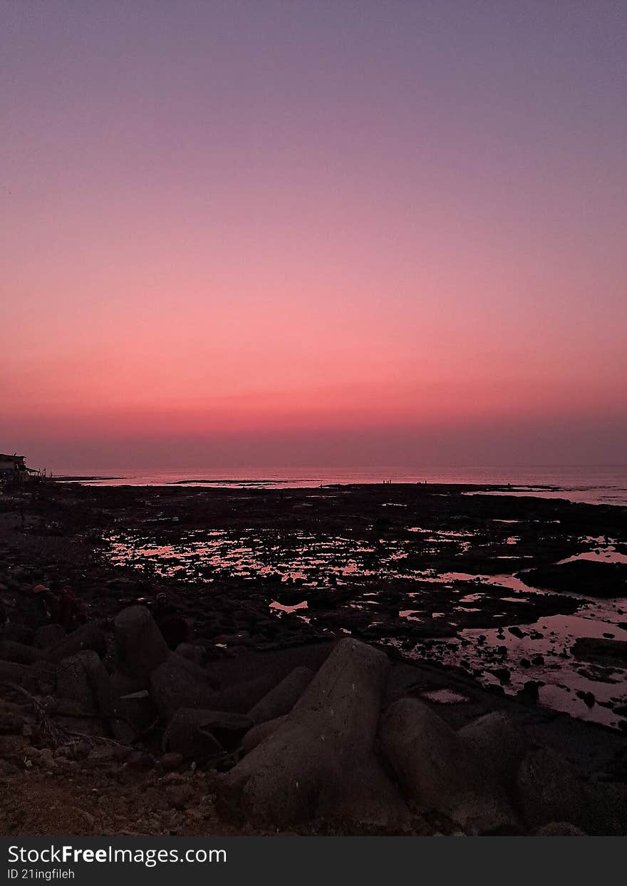 a sunset parting bright orange hues over a rocky sea shore