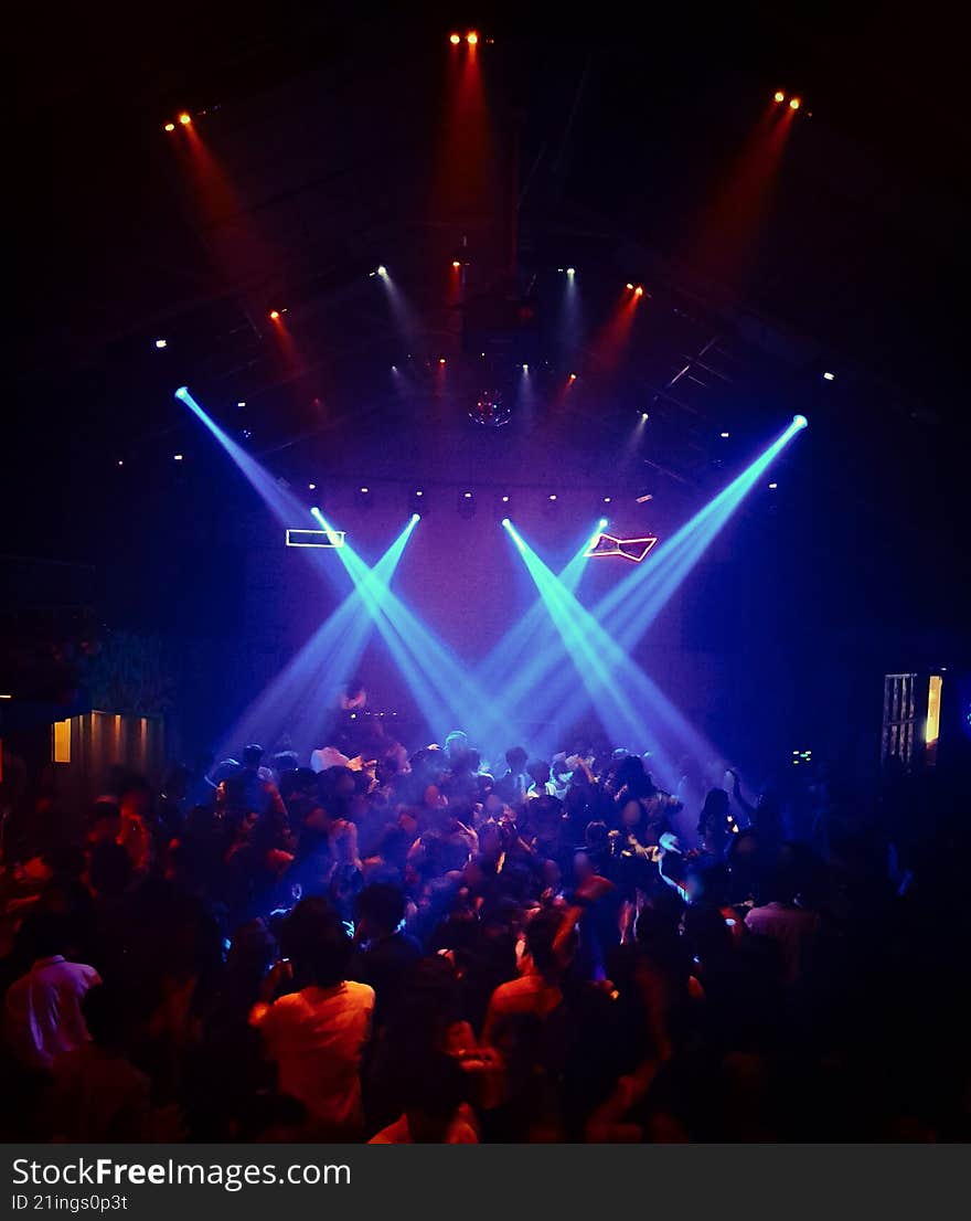 beams of blue and red spotlights falls over audience as they dance in a night club during a rock band concert