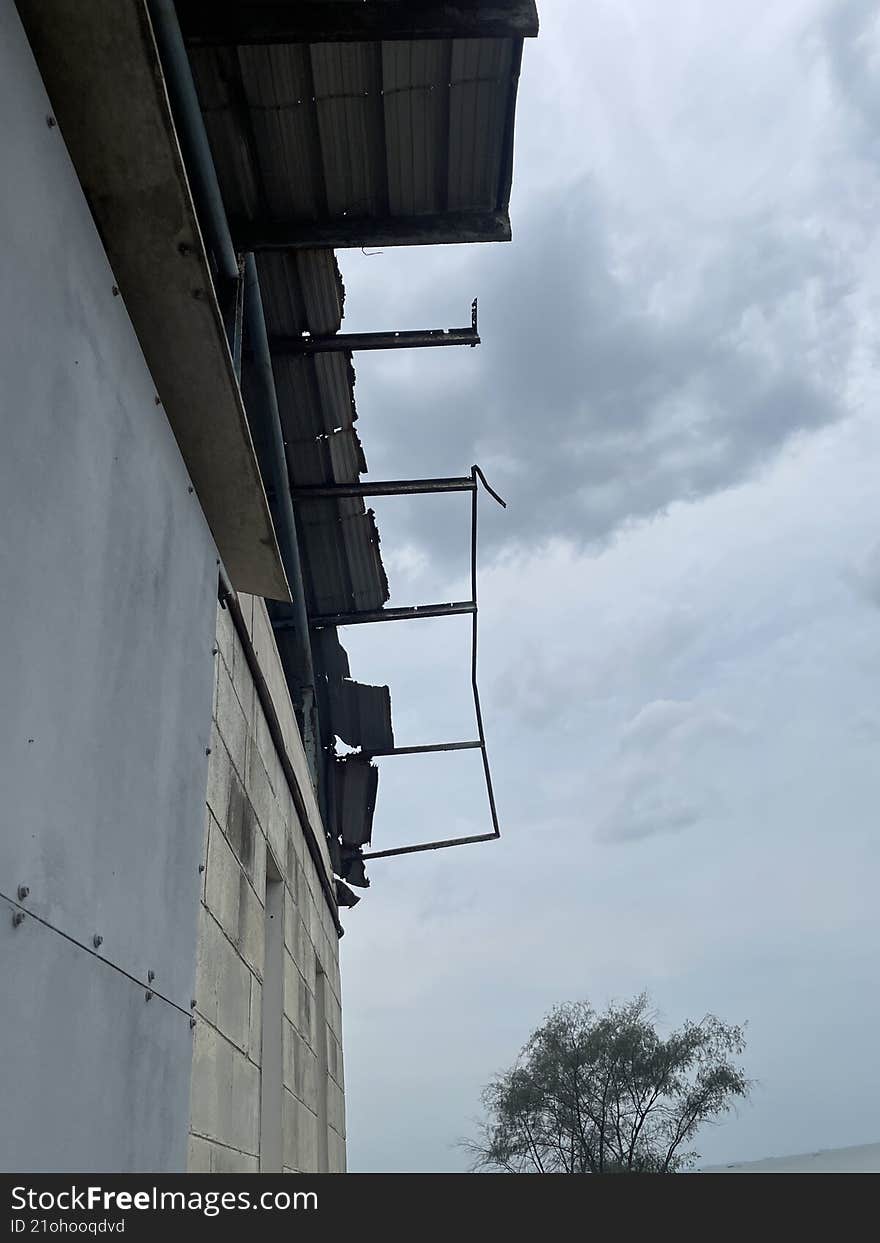 dilapidated roof structure of what appears to be an abandoned or unfinished building beneath an overcast sky. The dominant colors are gray and muted tones, conveying a somber and raw atmosphere. dilapidated roof structure of what appears to be an abandoned or unfinished building beneath an overcast sky. The dominant colors are gray and muted tones, conveying a somber and raw atmosphere