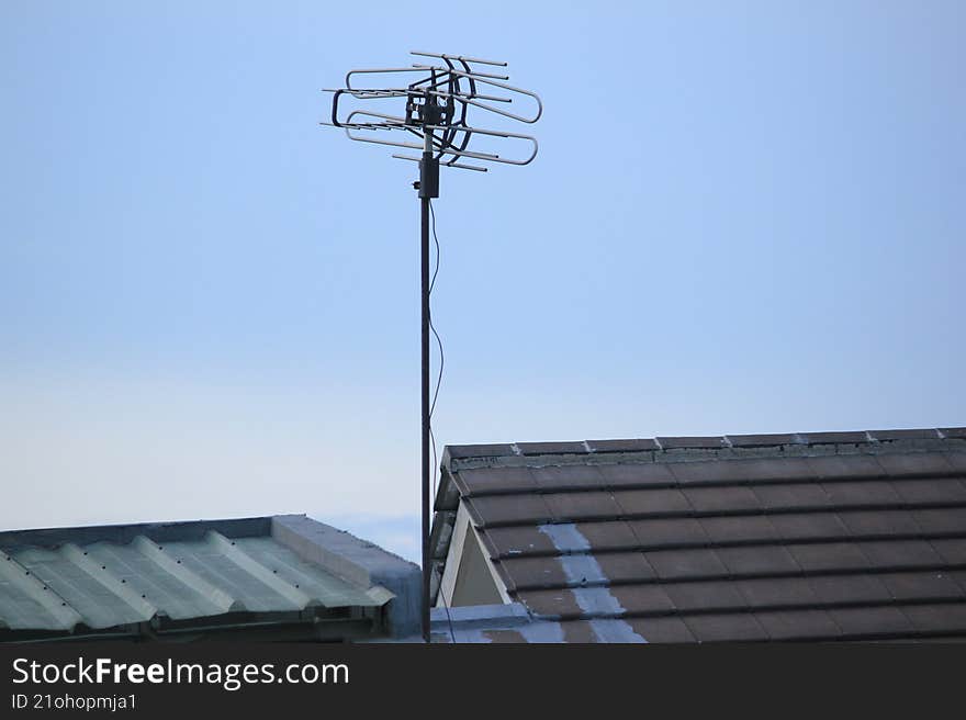 This image features a television antenna mounted on a house roof under a clear blue sky. The dominant colors are blue and gray, creating a simple and bright atmosphere. This image features a television antenna mounted on a house roof under a clear blue sky. The dominant colors are blue and gray, creating a simple and bright atmosphere