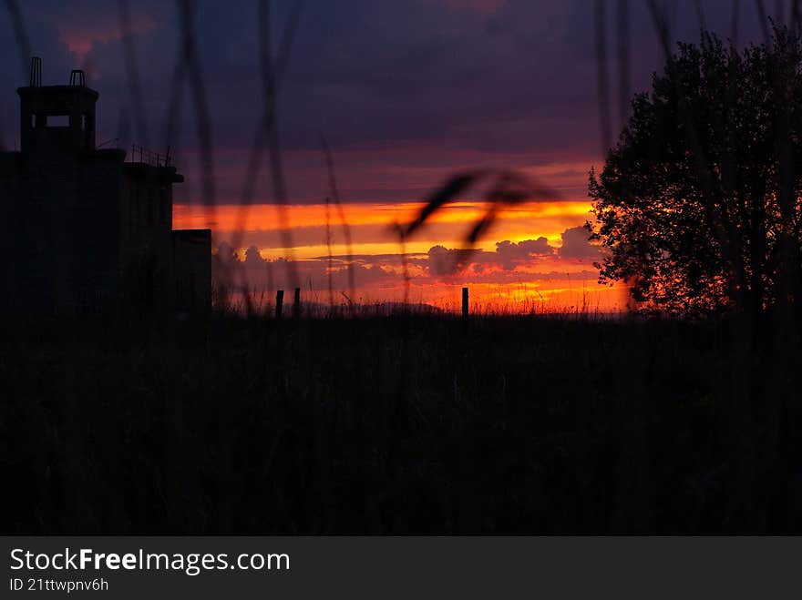 silhouette of a building and grass against the sunset sky