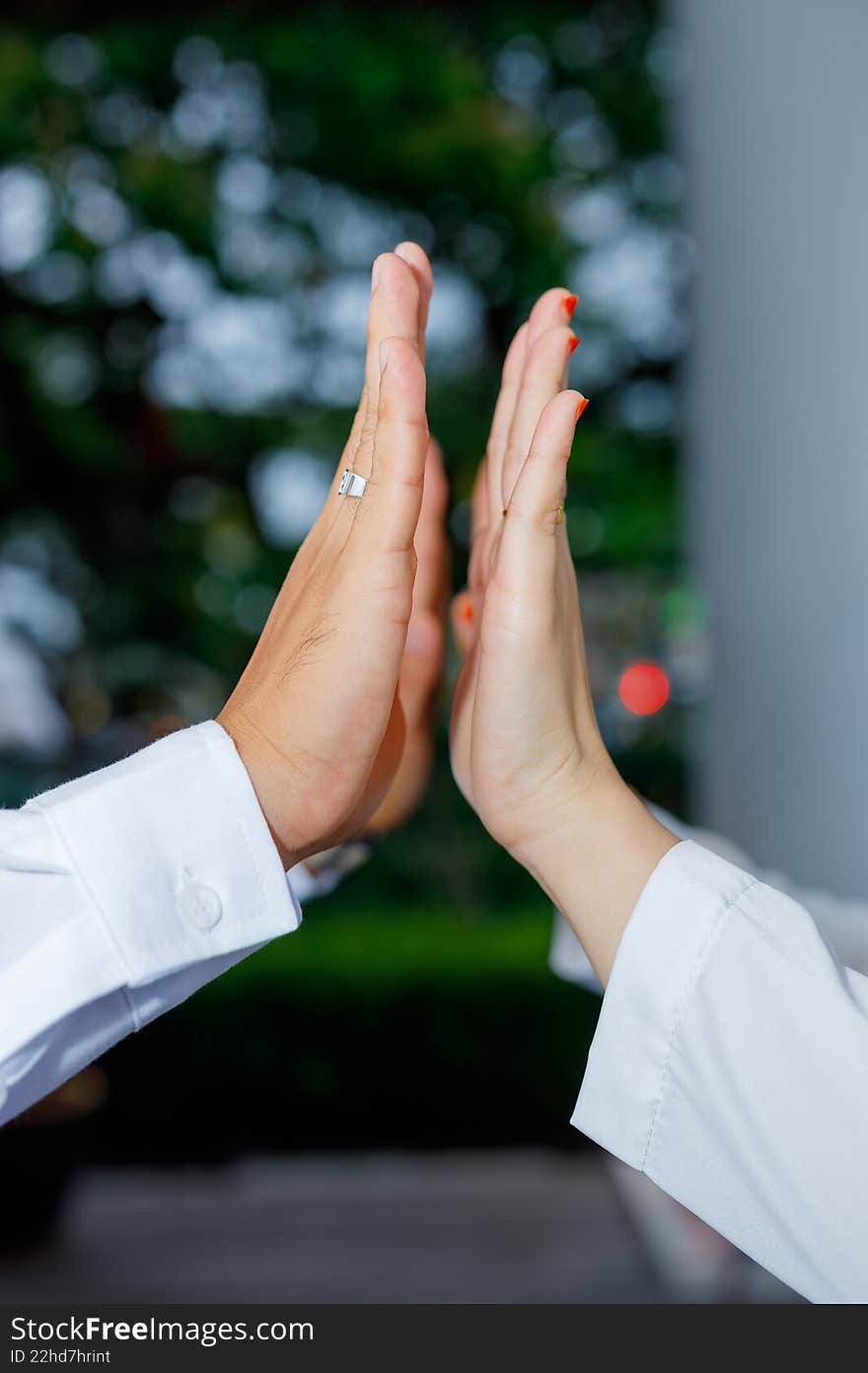 Close-up of a man and woman touching palms in a high-five or supportive gesture against a bokeh green background