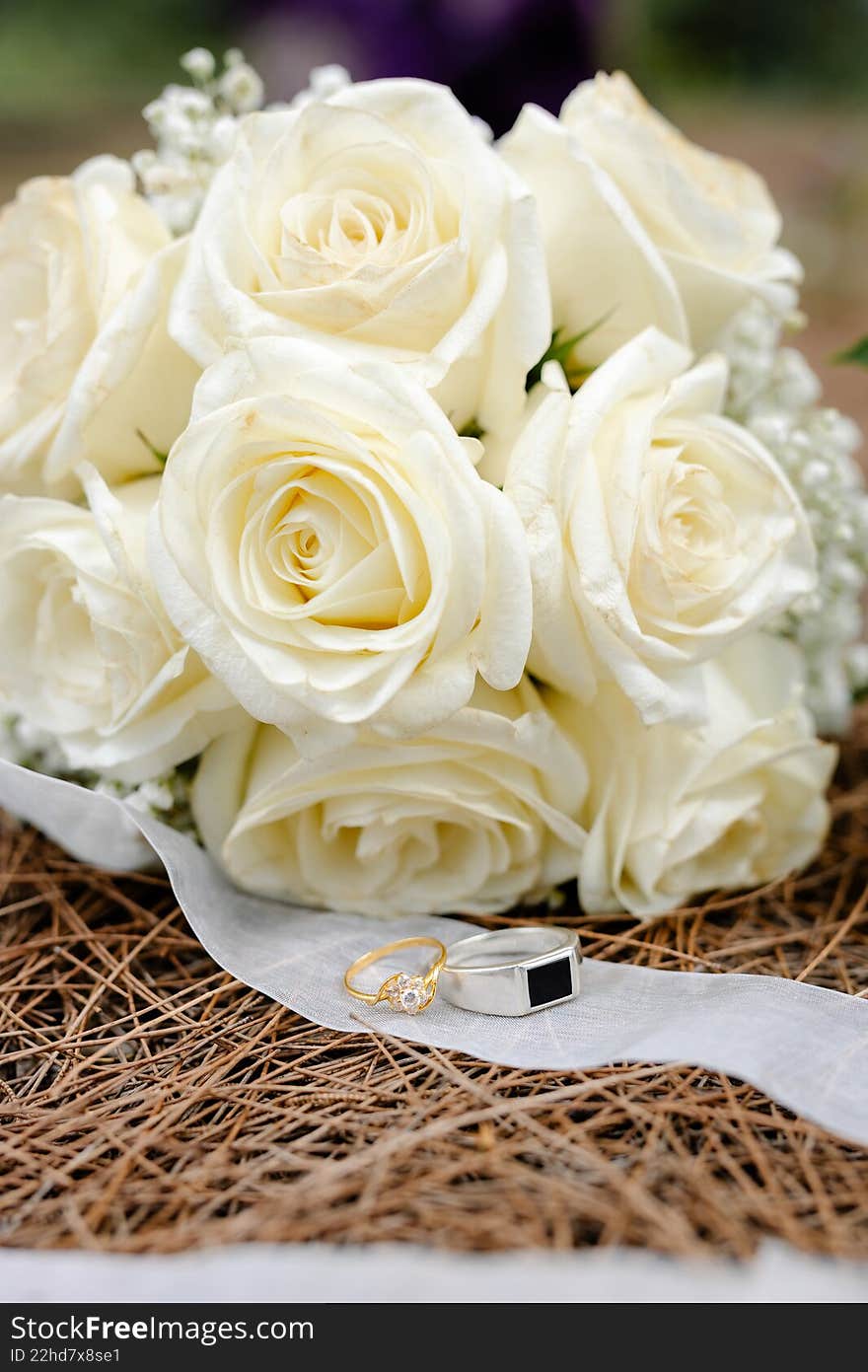 Two wedding rings sitting on a sheer ribbon in front of a large bouquet of fresh white roses