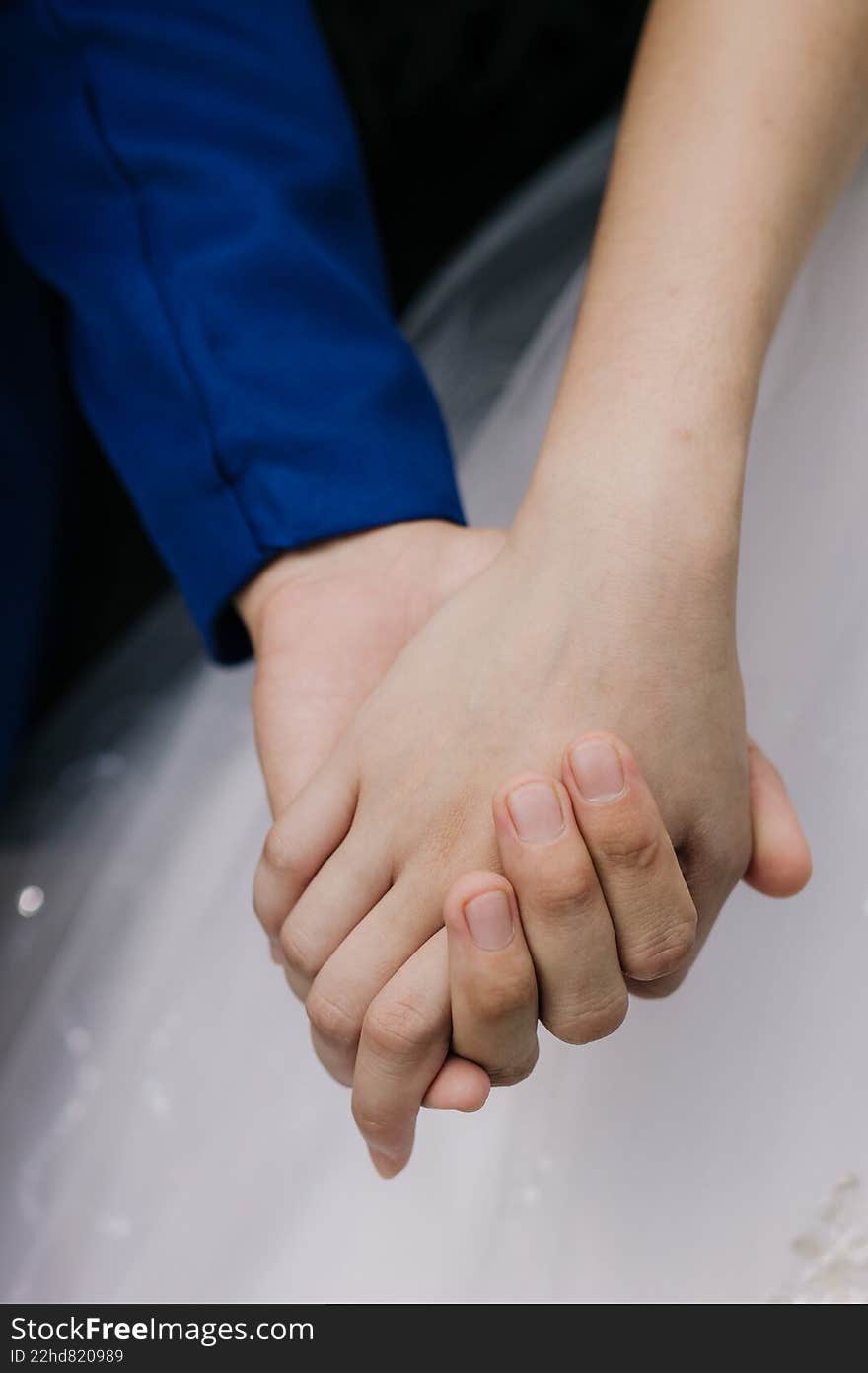A close up of a man and woman holding hands using blue shirt and gown background