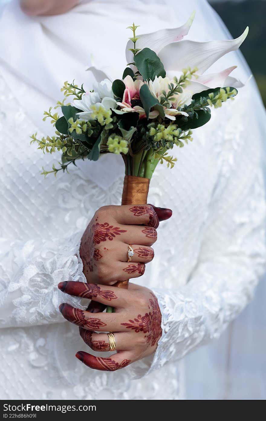 A close-up of a bride s hand adorned with intricate red henna holding a bouquet of pink lily
