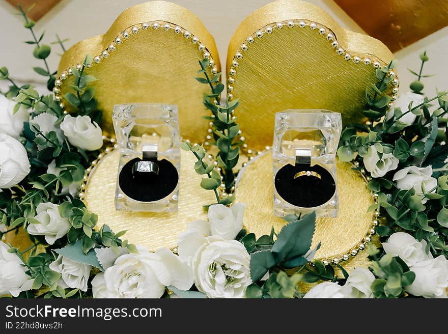 Two wedding rings displayed in clear boxes on gold heart-shaped