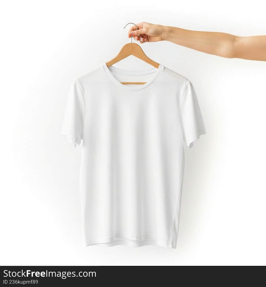 A studio-quality photograph captures a blank, plain white t-shirt hanging on a wooden clothes hanger. A person's hand is visible at the top, holding the hanger hook against a bright, isolated white background. The image is clean and minimalist, highlighting the garment and providing ample space for custom text or design mockups for clothing brands or online stores. A studio-quality photograph captures a blank, plain white t-shirt hanging on a wooden clothes hanger. A person's hand is visible at the top, holding the hanger hook against a bright, isolated white background. The image is clean and minimalist, highlighting the garment and providing ample space for custom text or design mockups for clothing brands or online stores
