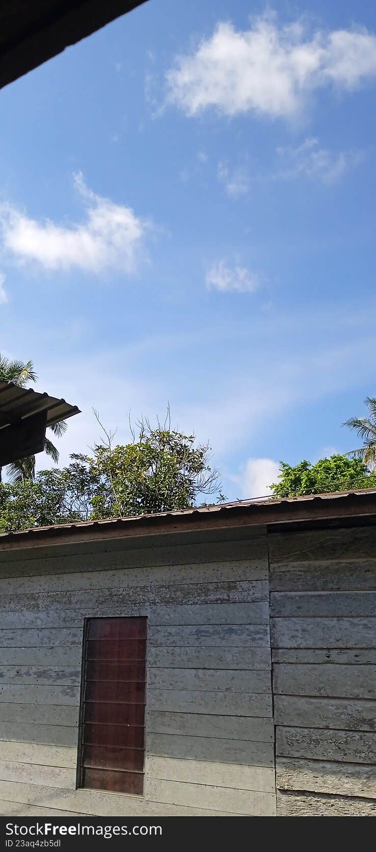 Traditional wooden house wall with a window under a clear blue sky with white clouds.