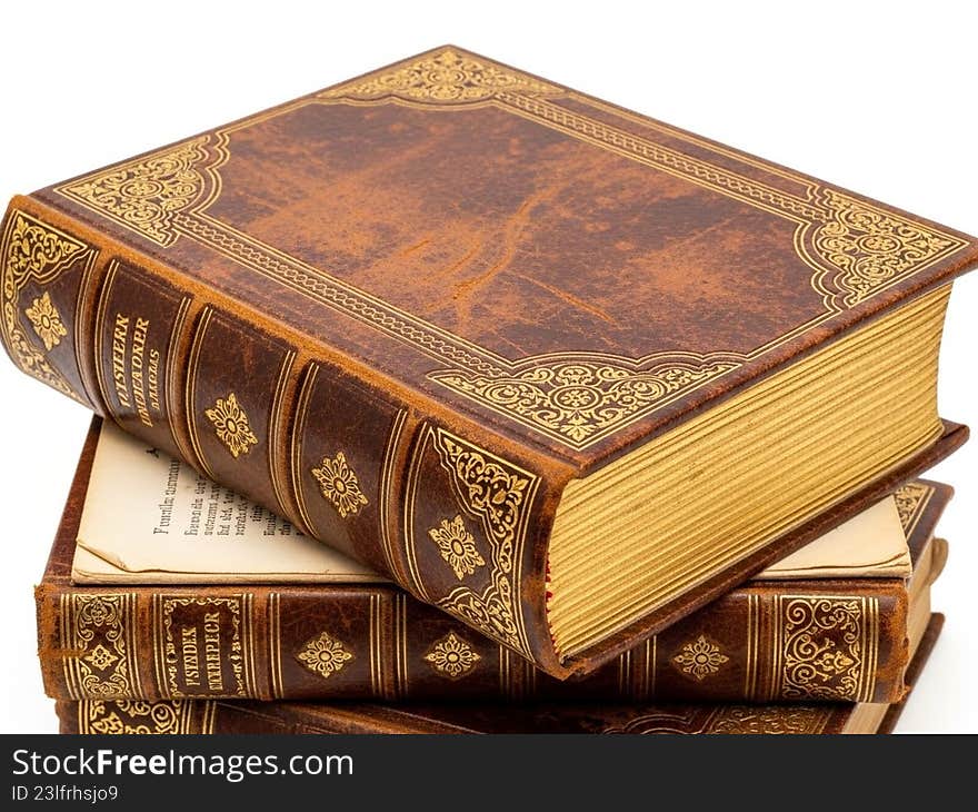 This image depicts a stack of three antique books with ornate, gold-embossed covers. The books are bound in rich, brown leather with intricate designs and patterns. The top book is slightly open, revealing yellowed pages with text. The overall appearance suggests a collection of classic or historical literature, evoking a sense of timeless knowledge and intellectual pursuit. This image depicts a stack of three antique books with ornate, gold-embossed covers. The books are bound in rich, brown leather with intricate designs and patterns. The top book is slightly open, revealing yellowed pages with text. The overall appearance suggests a collection of classic or historical literature, evoking a sense of timeless knowledge and intellectual pursuit