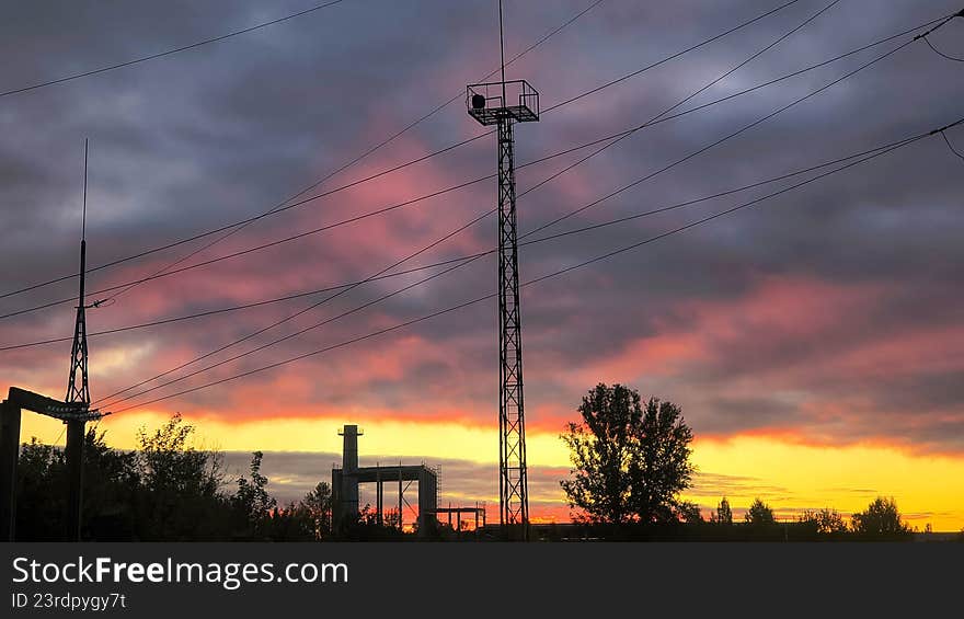 Industrial silhouettes standing under a vibrant, cloudy sky during either sunrise or sunset, conveying energy and infrastructure. Industrial silhouettes standing under a vibrant, cloudy sky during either sunrise or sunset, conveying energy and infrastructure