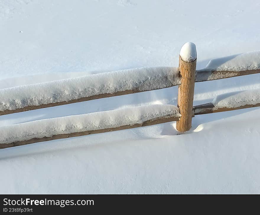 A high-angle view of a traditional wooden split-rail fence partially buried in a pristine, white snowfield. The crisp textures of the ice and snow against the natural wood create a peaceful, minimalist winter landscape perfect for seasonal background or nature-themed content.
