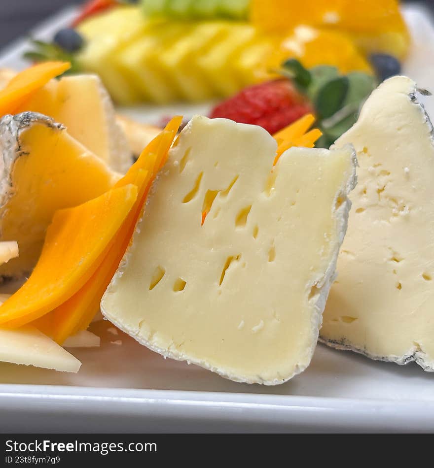 A sophisticated, close-up shot of a beautifully arranged appetizer platter. The image features a selection of fine cheeses, including creamy brie and sharp cheddar, alongside fresh strawberries, blueberries, citrus segments, and crisp breadsticks. This elegant composition is perfect for luxury catering marketing, wine pairing guides, hospitality brochures, or high-end food editorial content.
