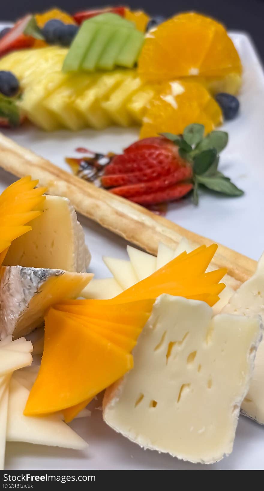 A sophisticated, close-up shot of a beautifully arranged appetizer platter. The image features a selection of fine cheeses, including creamy brie and sharp cheddar, alongside fresh strawberries, blueberries, citrus segments, and crisp breadsticks. This elegant composition is perfect for luxury catering marketing, wine pairing guides, hospitality brochures, or high-end food editorial content.
