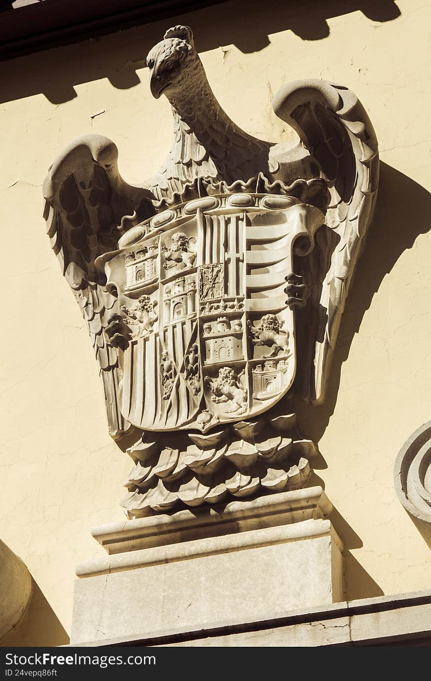 A detailed close-up of the three-dimensional coat of arms of Granada mounted on the facade of a historic building in Spain. The emblem features intricate sculptural elements, highlighting traditional heraldic motifs and craftsmanship typical of Andalusian architecture. Warm natural light emphasizes the texture of the stone surface and the depth of the carved relief, creating a striking visual contrast. The composition reflects the cultural heritage and artistic identity of Granada, making the image suitable for travel-related content, architectural editorials, cultural documentation, or projects focused on Spanish history and design. A detailed close-up of the three-dimensional coat of arms of Granada mounted on the facade of a historic building in Spain. The emblem features intricate sculptural elements, highlighting traditional heraldic motifs and craftsmanship typical of Andalusian architecture. Warm natural light emphasizes the texture of the stone surface and the depth of the carved relief, creating a striking visual contrast. The composition reflects the cultural heritage and artistic identity of Granada, making the image suitable for travel-related content, architectural editorials, cultural documentation, or projects focused on Spanish history and design.