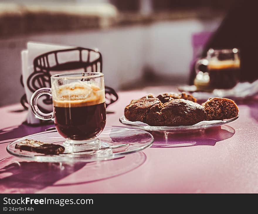 Espresso Coffee and Fresh Pastries on a Sunlit Caf� Table - Close-up of a freshly brewed espresso served in a glass cup alongside