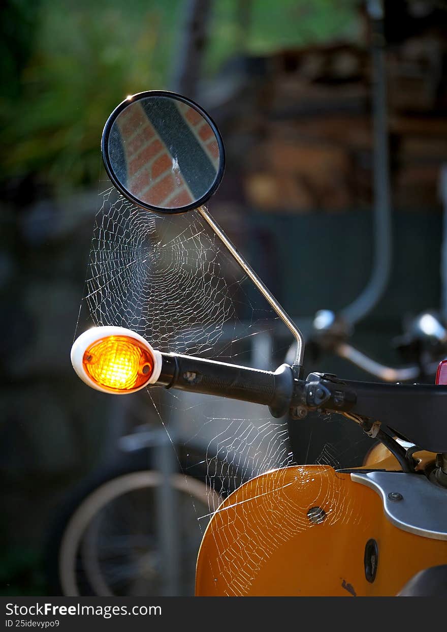 Spider web covering an old orange scooter handlebar, mirror, and signal light