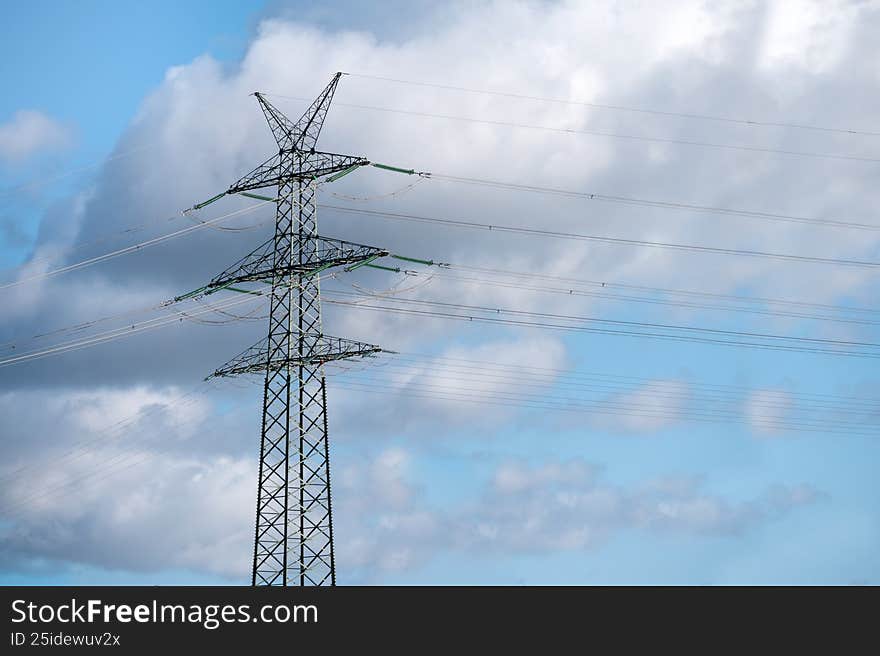 Electricity transmission pylon supporting power lines connecting networks against a blue sky with clouds