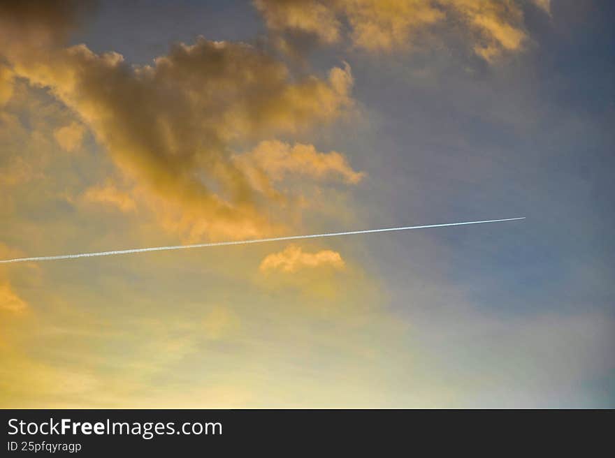 Airplane contrail crossing a warm golden sunset sky with illuminated clouds. Minimal atmospheric background with soft evening ligh