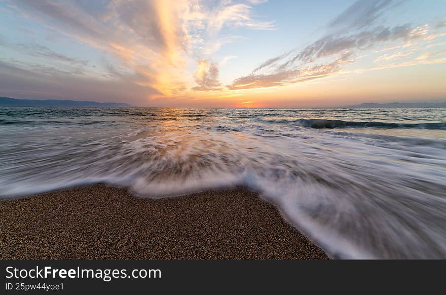 A Colorful Sunset Seascape With A Wave Flowing Over Sand