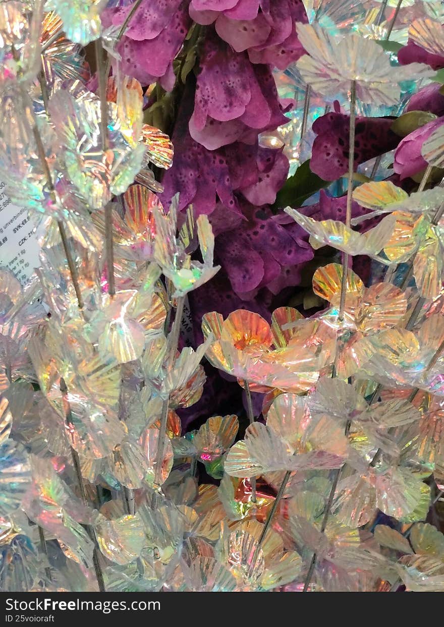 Close-up of iridescent artificial flowers with holographic reflective surface and purple floral accents. Decorative ornamental arrangement with shimmering light reflections and abstract texture. Fantasy inspired design background. Close-up of iridescent artificial flowers with holographic reflective surface and purple floral accents. Decorative ornamental arrangement with shimmering light reflections and abstract texture. Fantasy inspired design background.