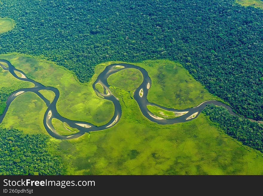 This aerial photograph captures a serene and vibrant landscape featuring a winding river that flows through a lush green forest. T