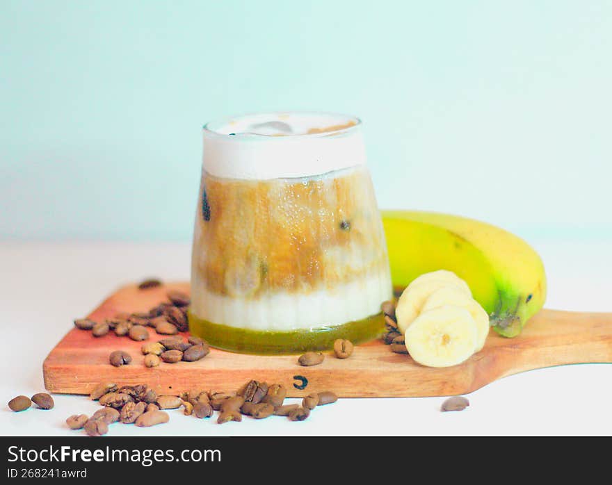 Close-up shot of a glass of banana juice mixed with a little coffee and beside the glass there are sliced ??bananas and a whole banana.